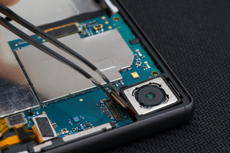 Fotografia 1. Wnętrze smartfona z widocznymi taśmami FPC (uniesiona pęsetą część ukazuje gniazdo Mezzanine znajdujące się na PCB tuż obok modułu kamery)