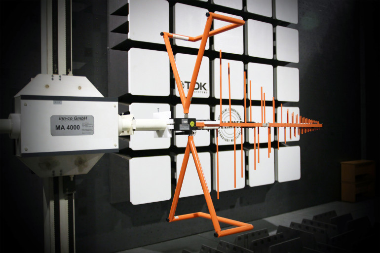 Fotografia 2. Wnętrze komory SAC – widoczna antena pomiarowa na kolumnie zmotoryzowanej oraz absorbery elektromagnetyczne (w tle)